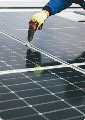Worker wearing a glove using a power drill to install solar panels.