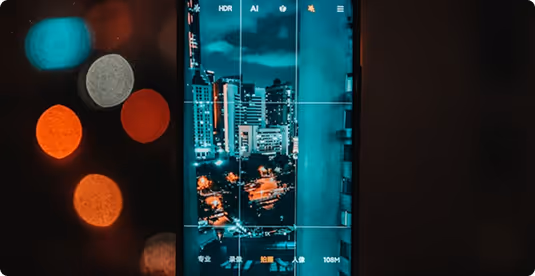 Smartphone screen displaying a nighttime cityscape being photographed, with buildings and streetlights visible.