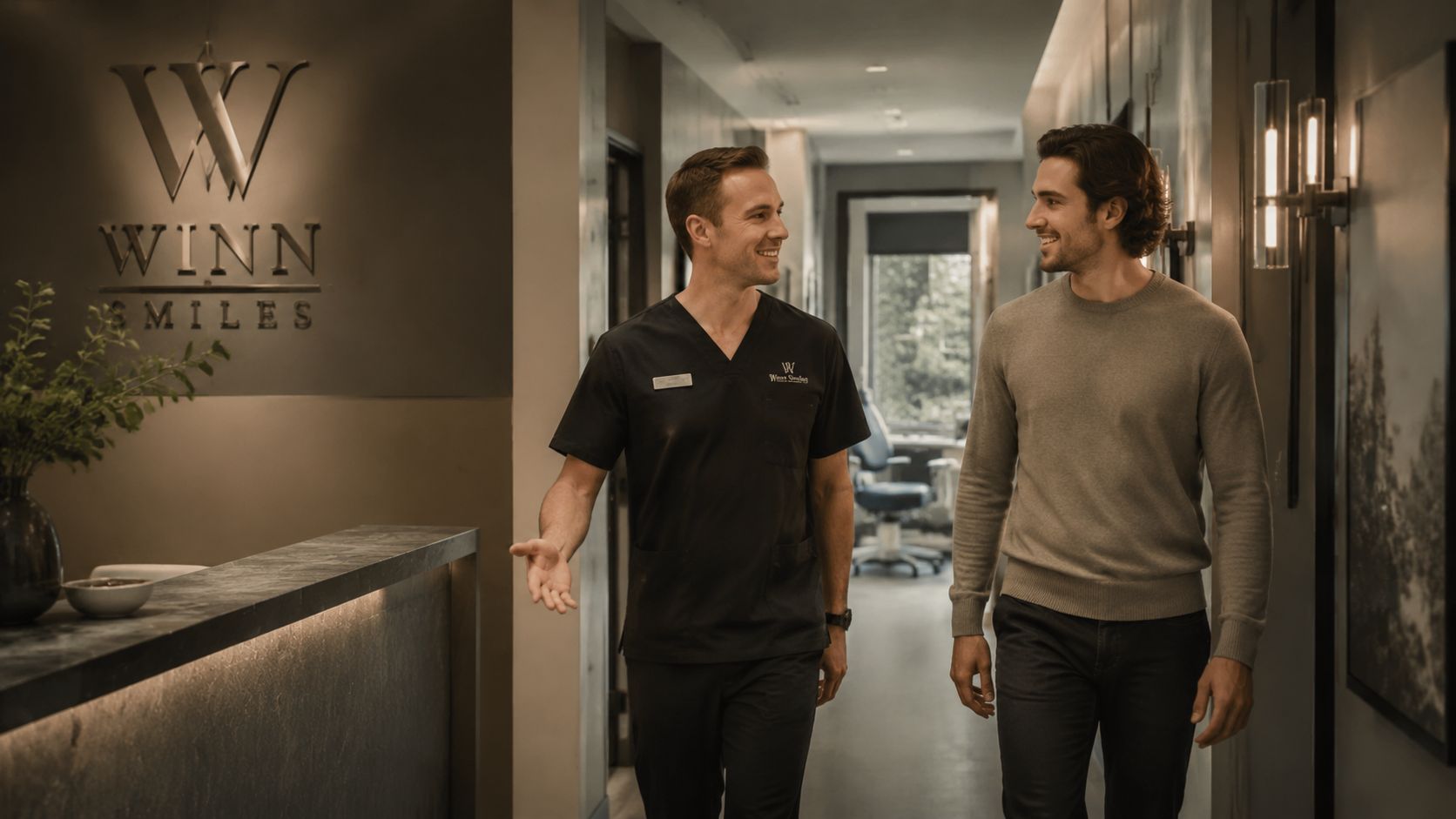 A smiling dentist in scrubs greets a patient in a modern professional dental clinic office hallway.
