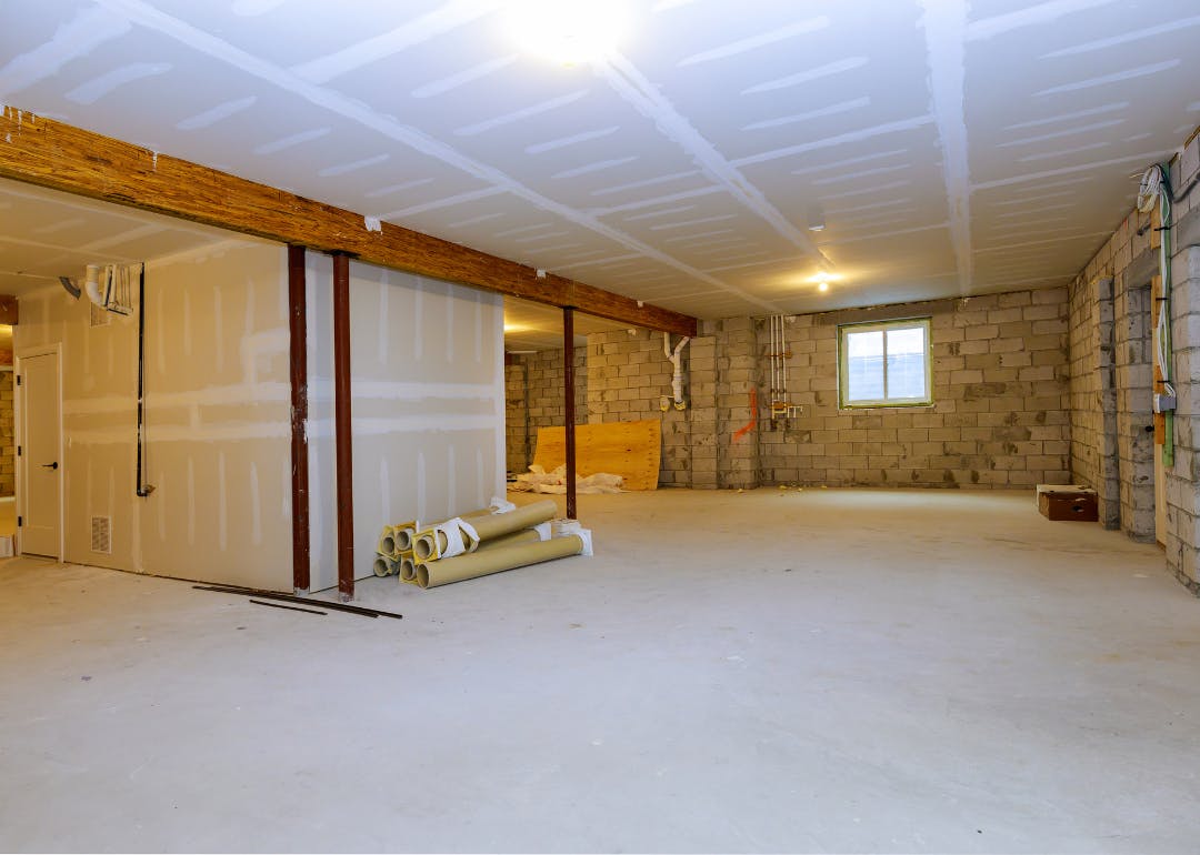 Unfinished basement under renovation with exposed walls, beams, and construction materials.