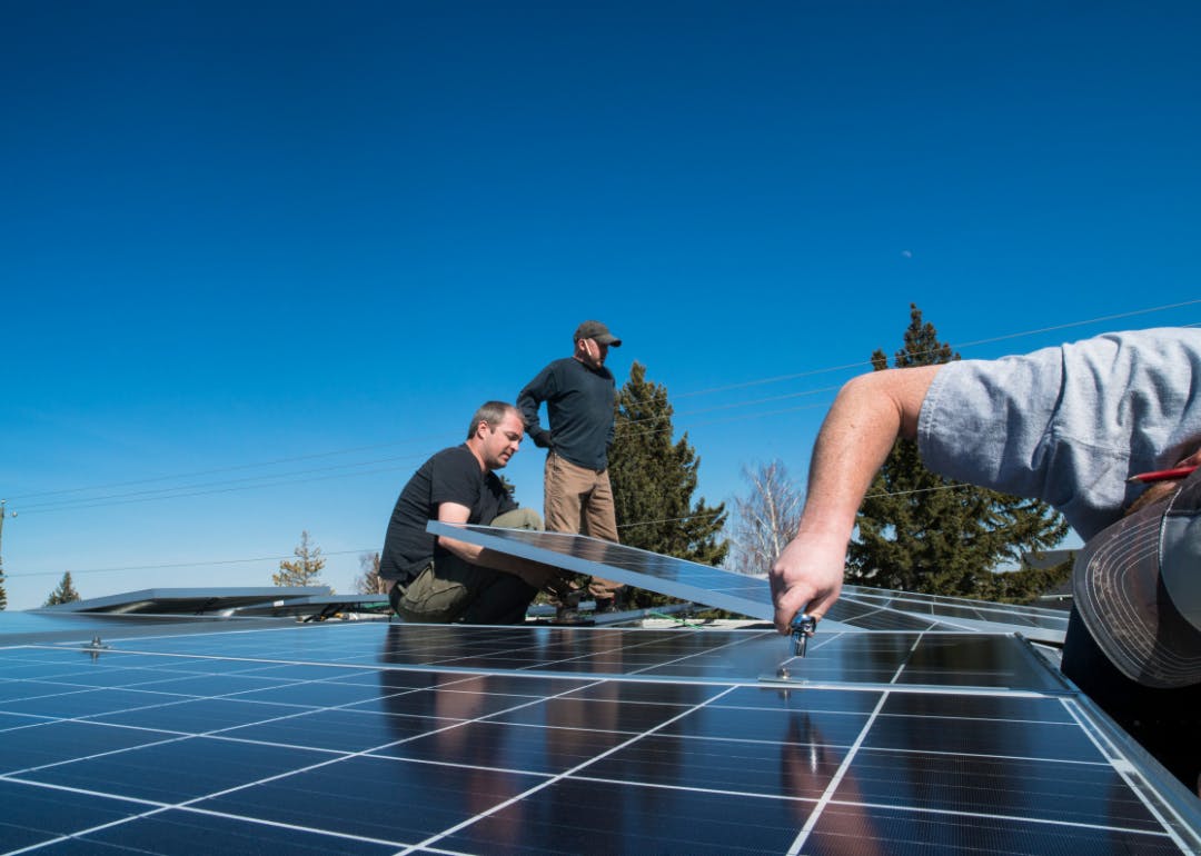 Workers installing solar panels on a rooftop under a clear blue sky.
