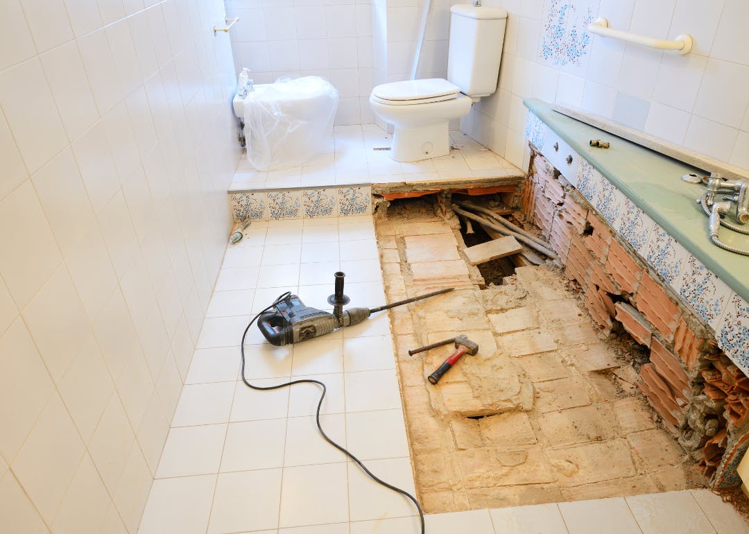 Bathroom under renovation with floor tiles removed and exposed plumbing.