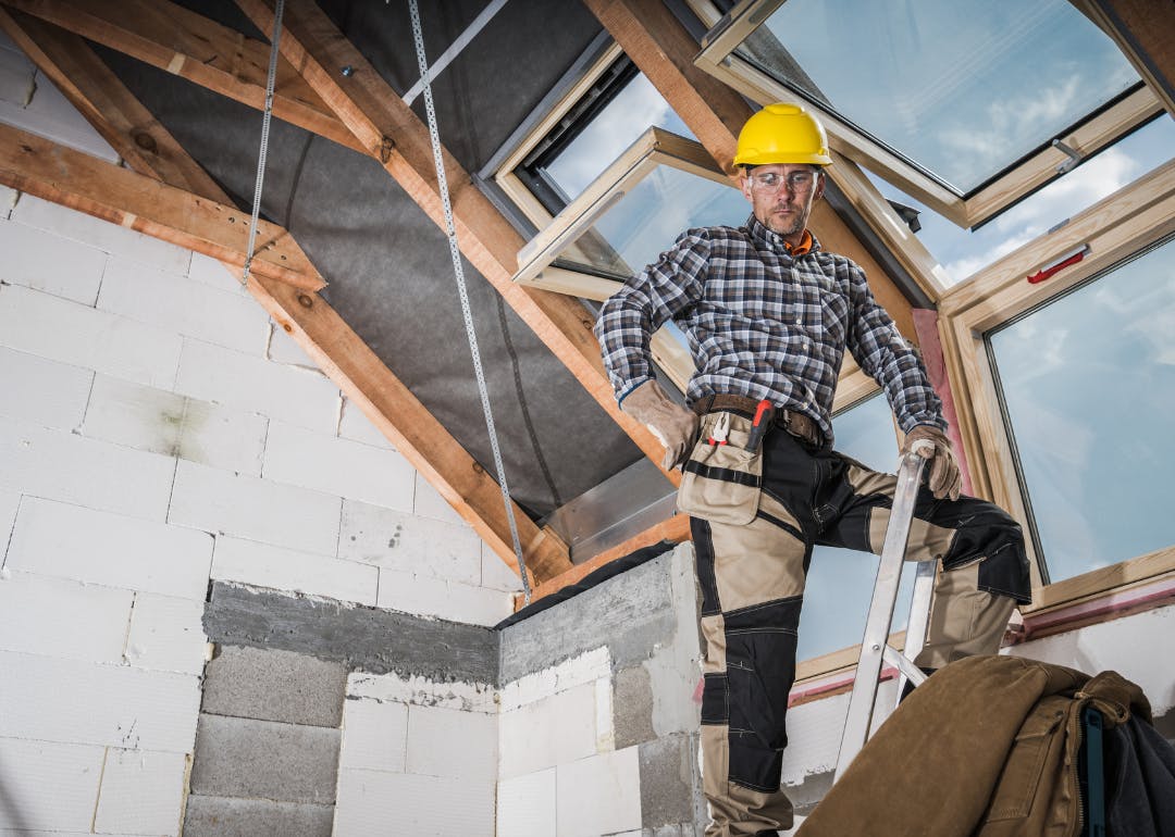 Construction worker on a ladder installing skylight windows during a home renovation.
