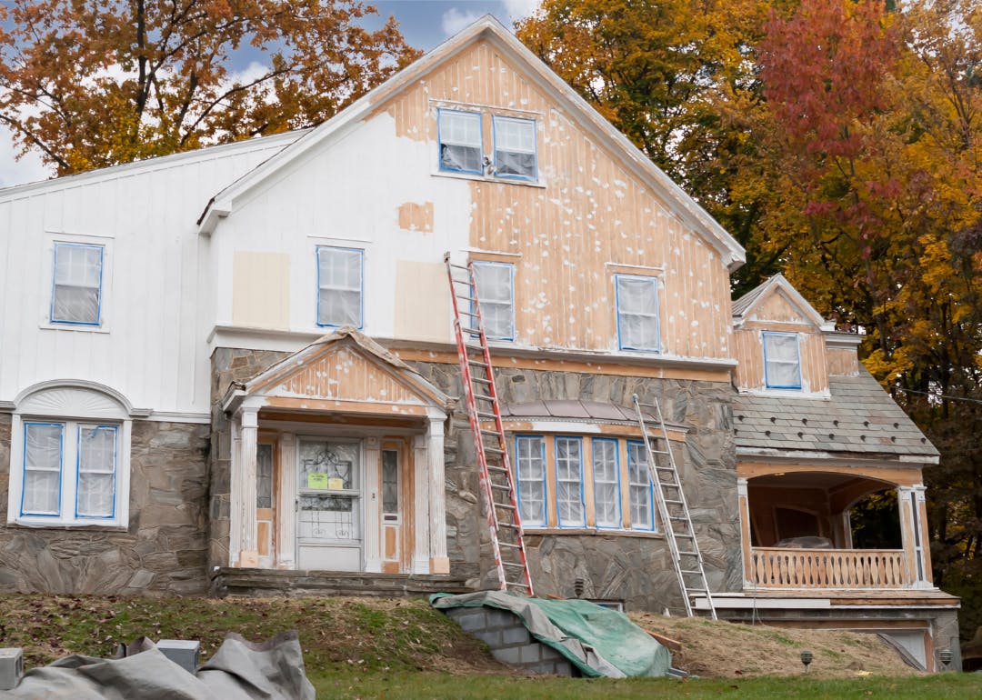 House exterior under renovation with ladders set up and preparation for painting.