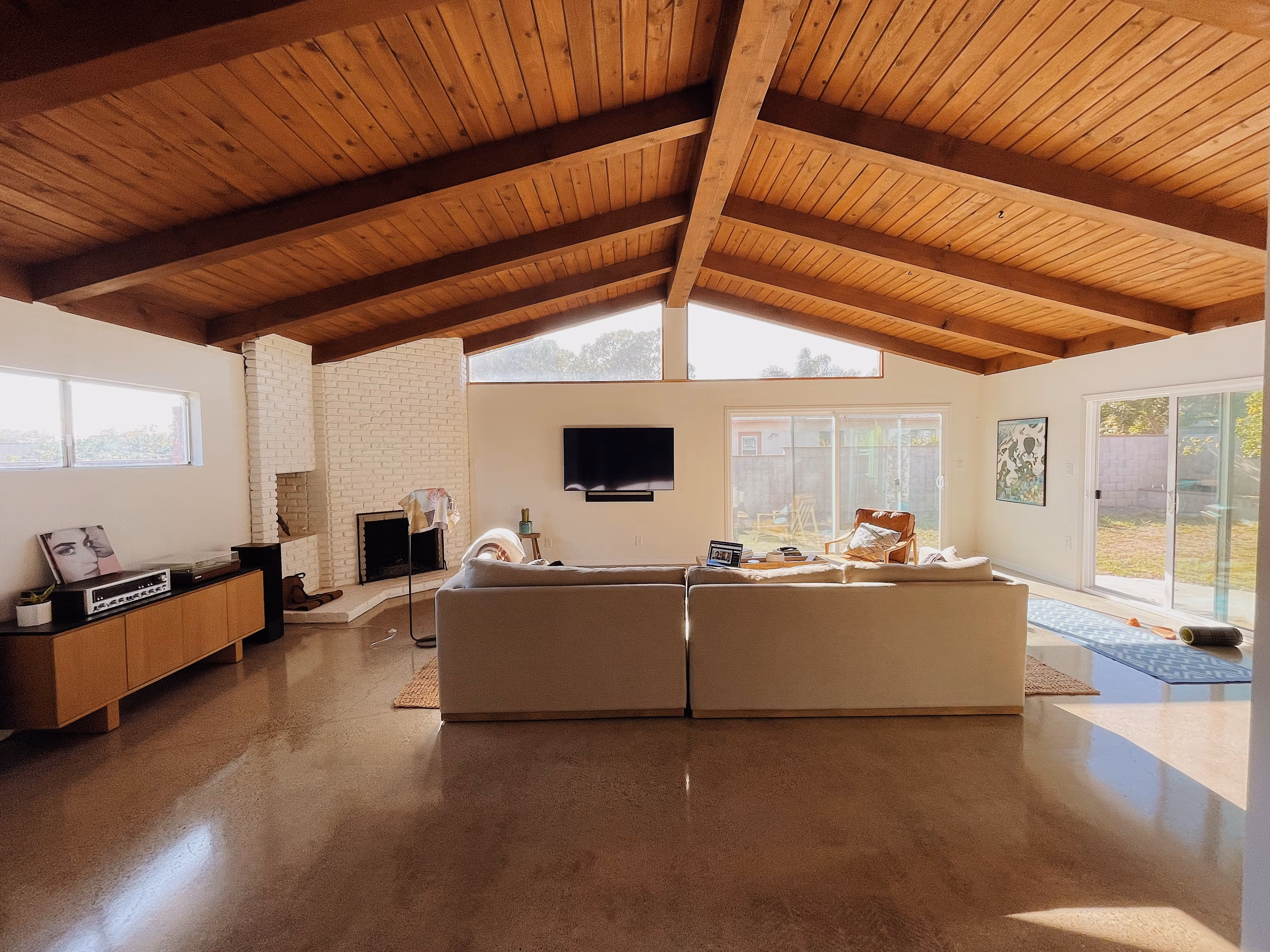 Spacious living room with vaulted wooden ceilings, a white brick fireplace, and large sliding glass doors.