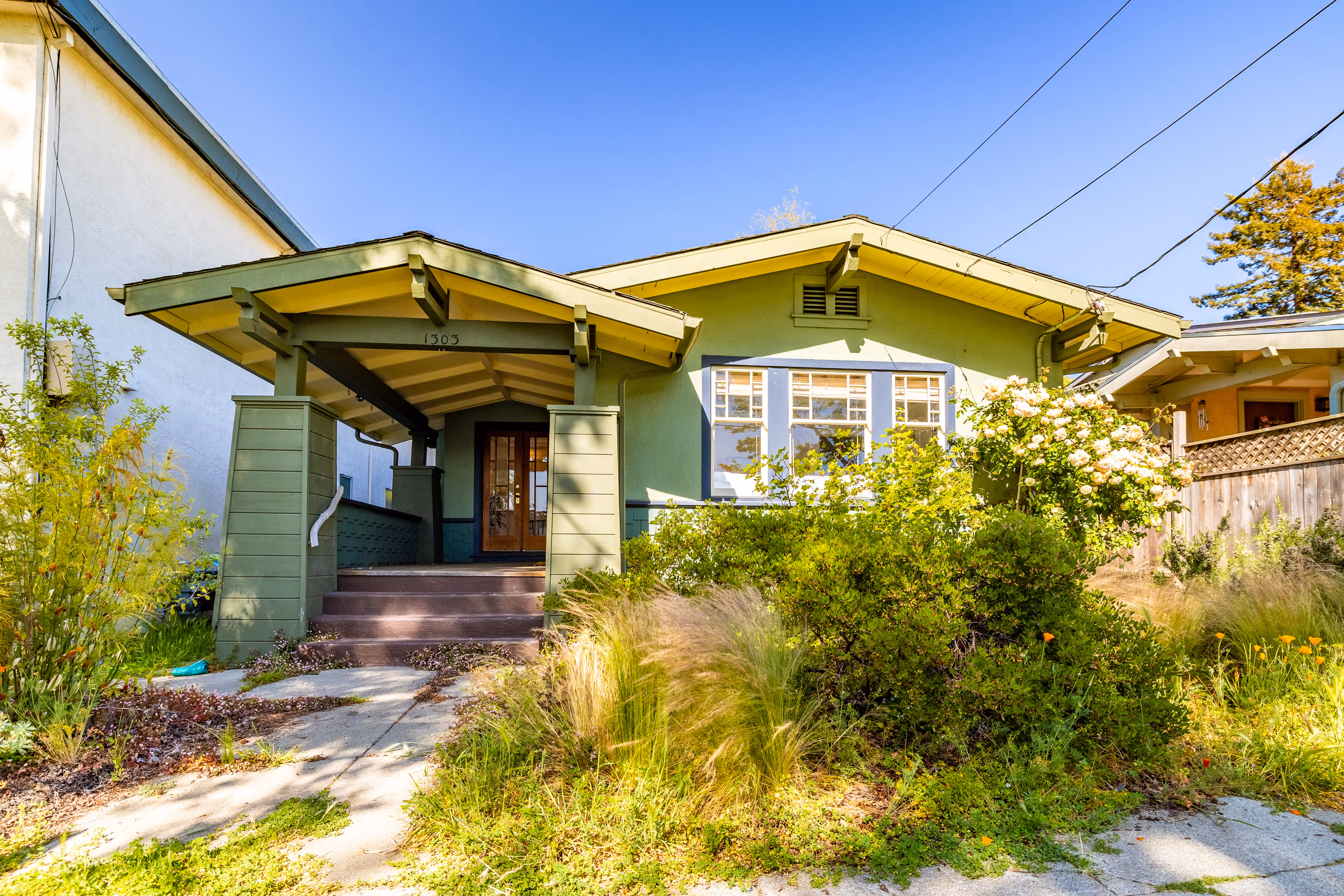 Green craftsman-style house with a covered porch and lush front garden.