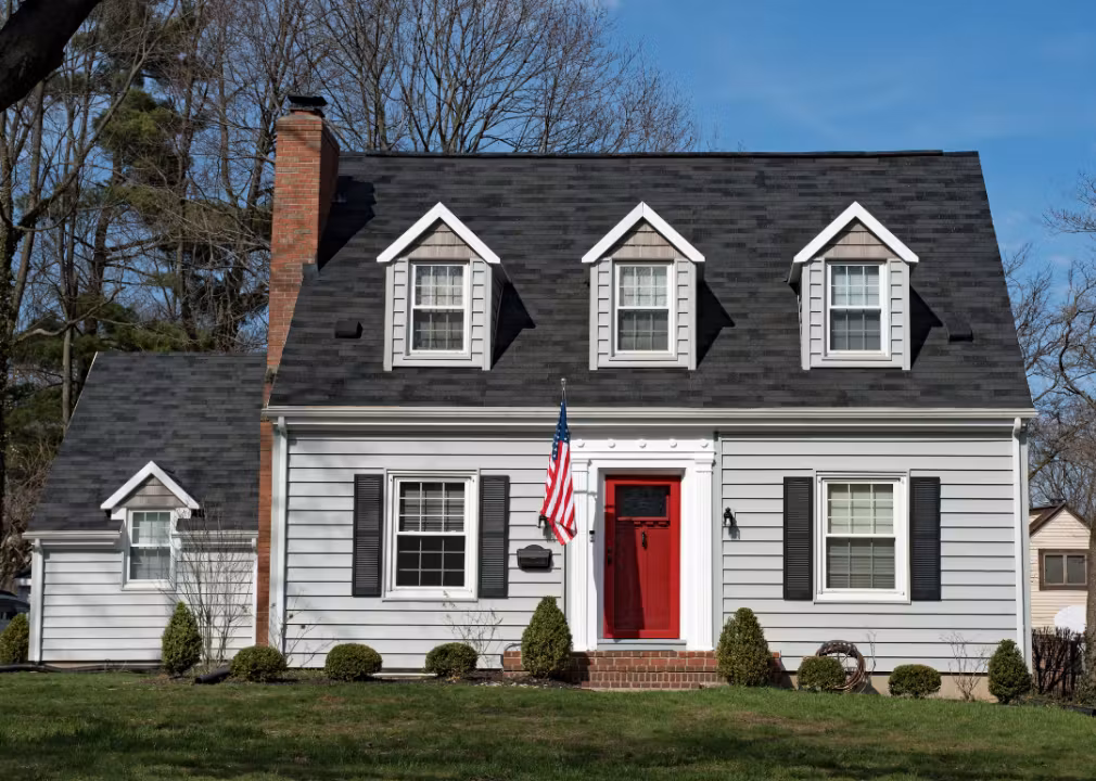 Traditional Cape Cod style house with gray siding, black shutters, and a red front door.