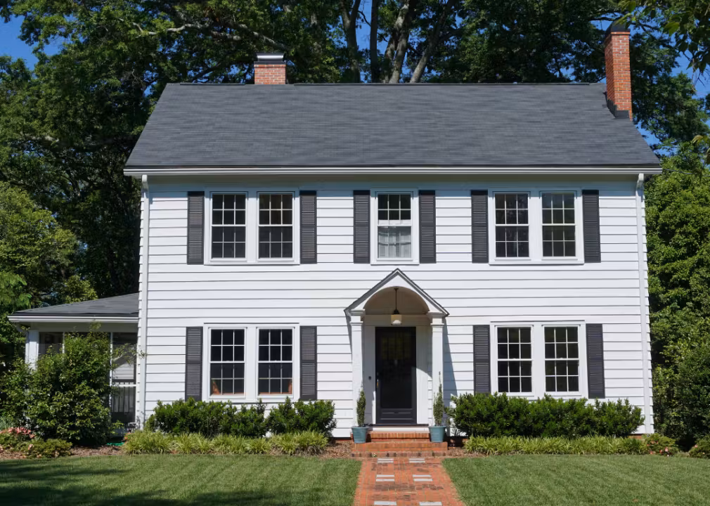 Two-story colonial-style house with white siding, black shutters, and a central front entrance.