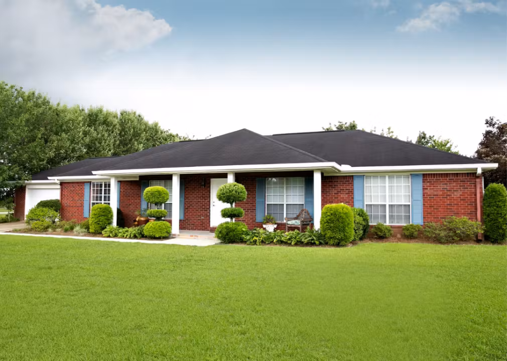 Single-story ranch-style brick house with blue shutters and a neatly landscaped front yard.