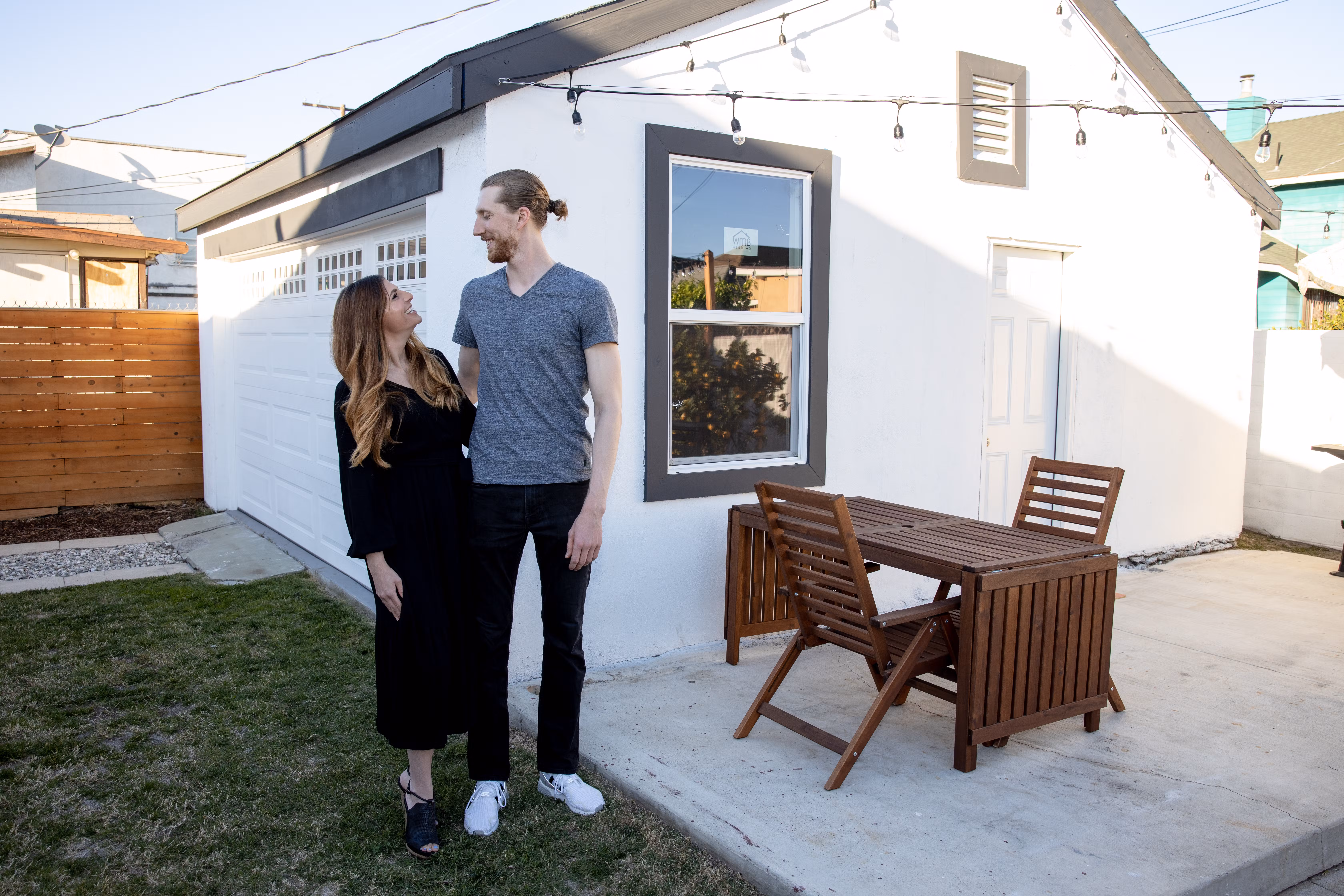 Smiling couple standing together in the backyard beside a white ADU with a patio table.