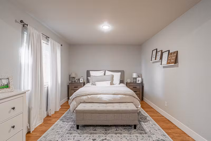 Cozy bedroom with a neatly made bed, matching nightstands, and soft neutral decor.