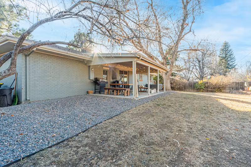 A backyard view of a house with a covered patio, outdoor seating, and surrounding trees.