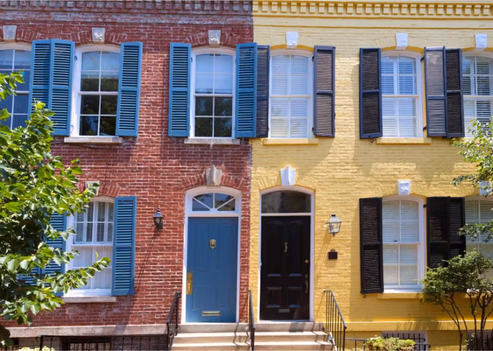 Two colorful row houses side by side, one with red brick and blue shutters and the other with yellow brick and black shutters.