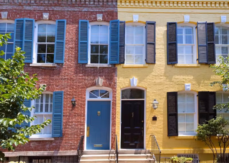 Two colorful row houses side by side, one with red brick and blue shutters and the other with yellow brick and black shutters.