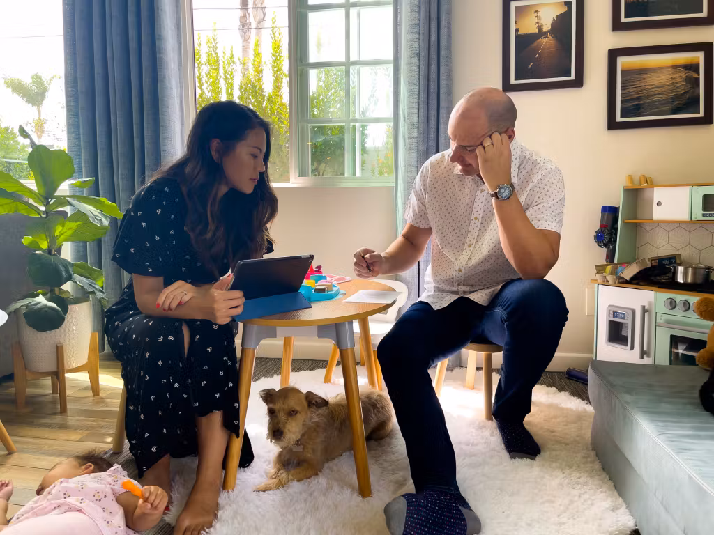 Couple sitting at a small table reviewing documents together while a dog rests at their feet.