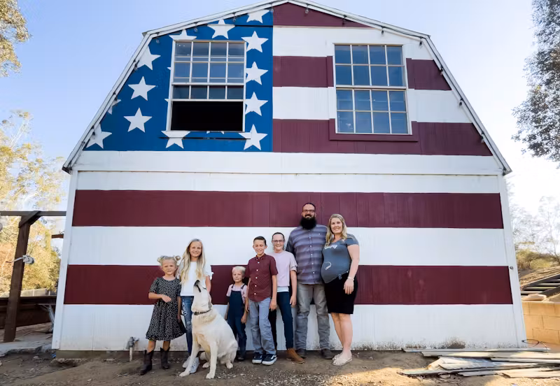 Family with children and a dog posing in front of a barn painted like the American flag.
