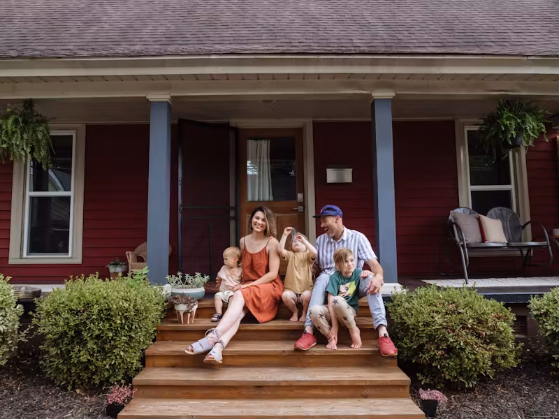 Family sitting together on the front steps of their red house, enjoying time outdoors.
