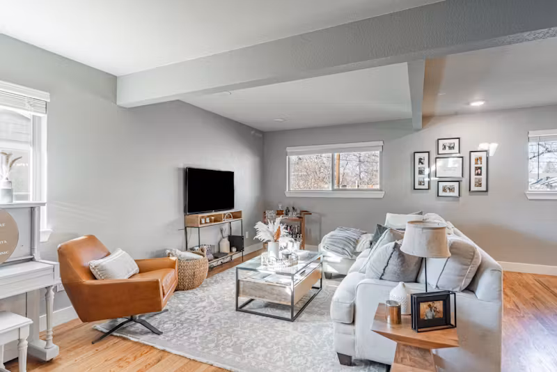 Bright, modern living room with gray walls, cozy seating, and natural light streaming through multiple windows.
