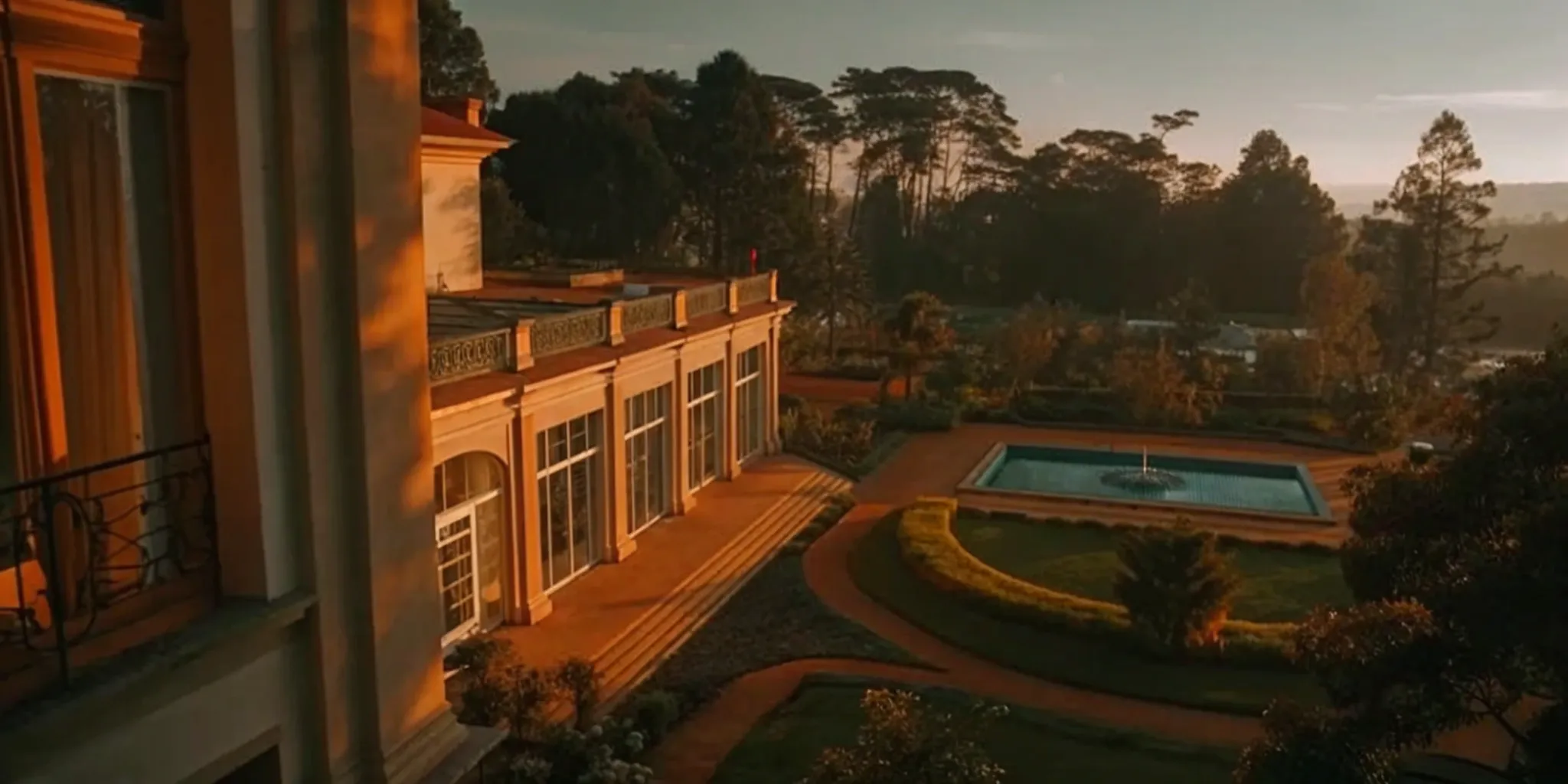 Luxury 10,000 sq ft house with a manicured garden and pool at sunset.