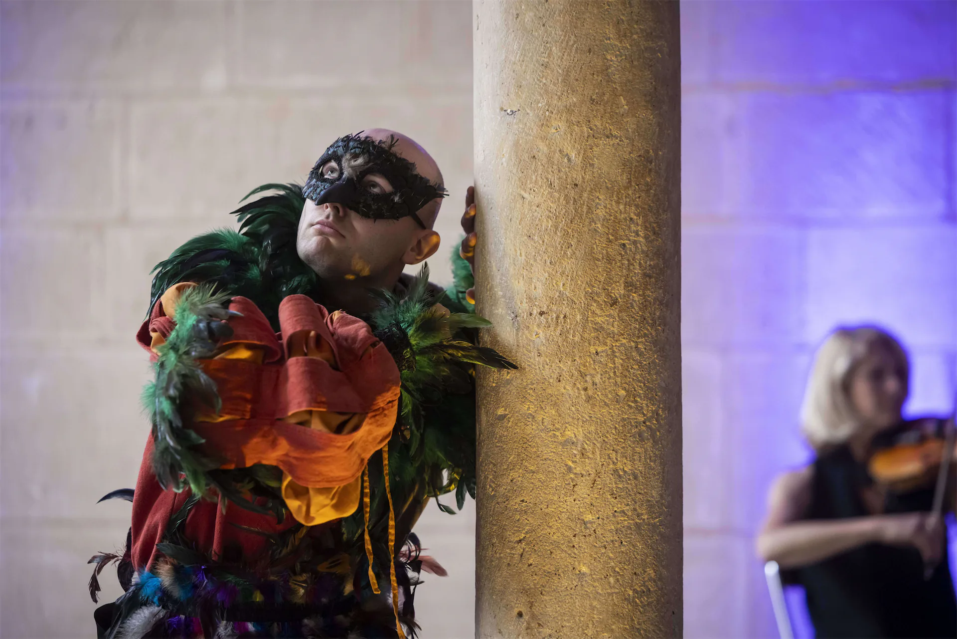 Comédiens masqué et violoniste en costumes d’époque baroque exécutant une chorégraphie colorée sous les arches d’une salle voûtée, dans le cadre du spectacle Le Mystère Mozart.