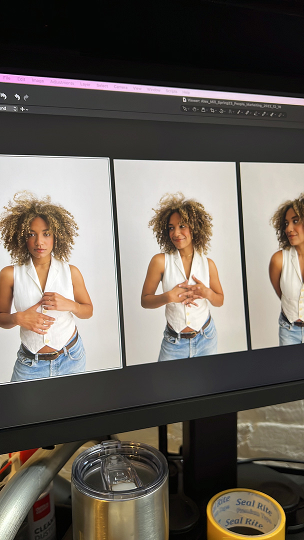 A computer screen showing a Capture One editing session with Natalie Wright modeling for Alex Mill. She is wearing a fitted white vest, light-wash denim jeans, and a brown leather belt. The images capture her expressive poses and natural curly hair against a clean white backdrop.