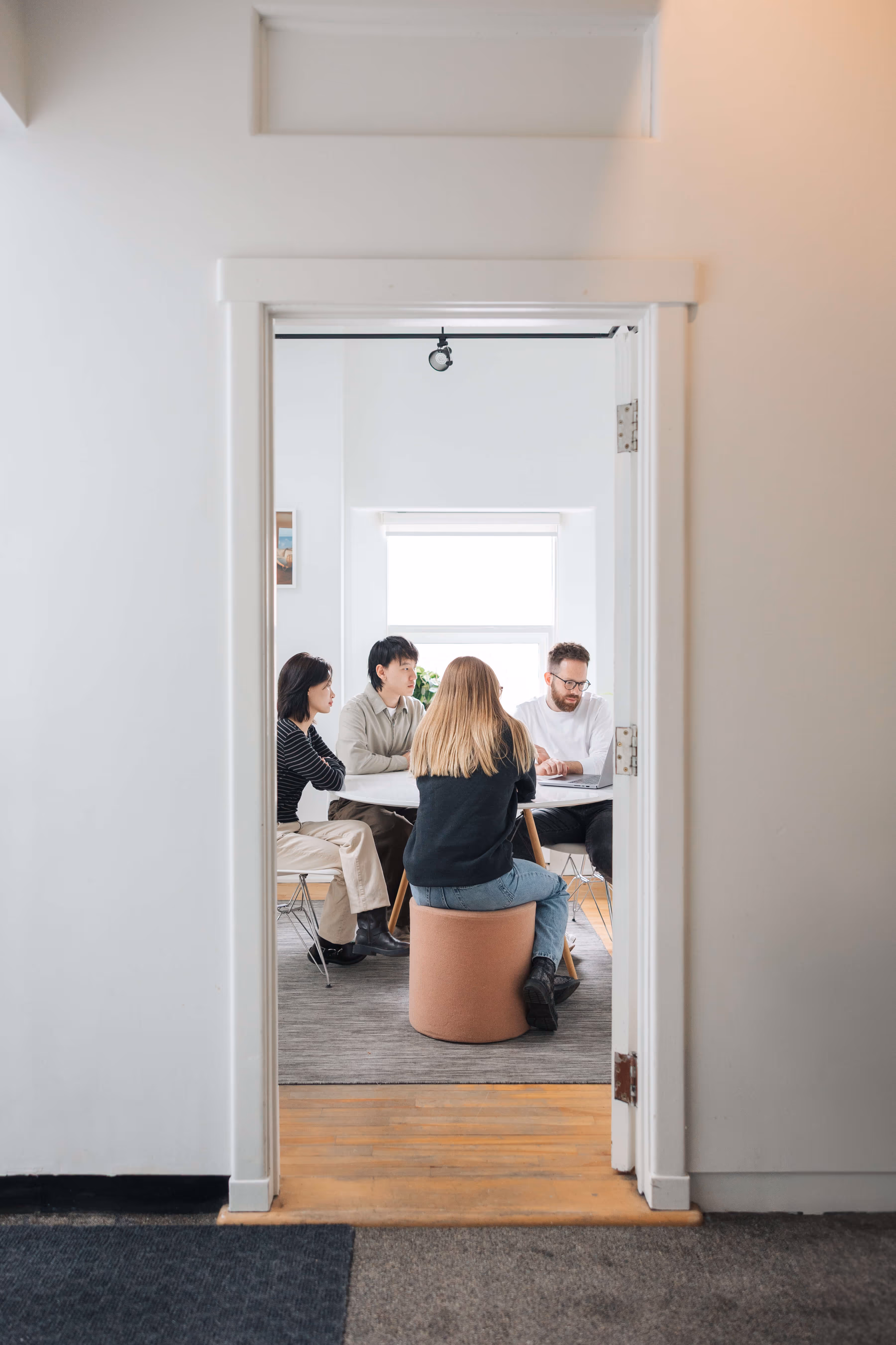 Four people sitting around a table in a bright room, engaged in a discussion with a laptop.