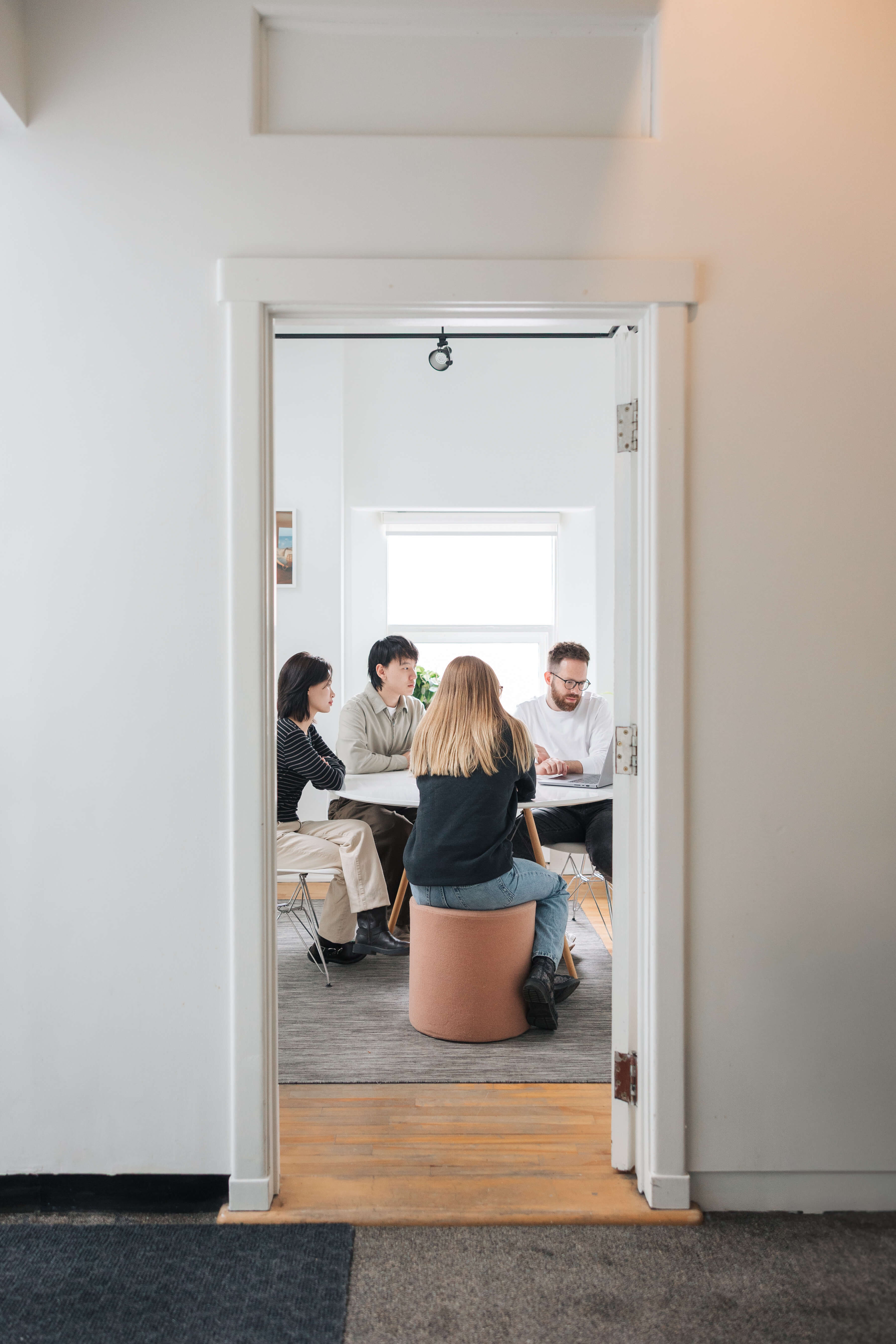 Four people sitting around a table in a bright room, engaged in a discussion with a laptop.