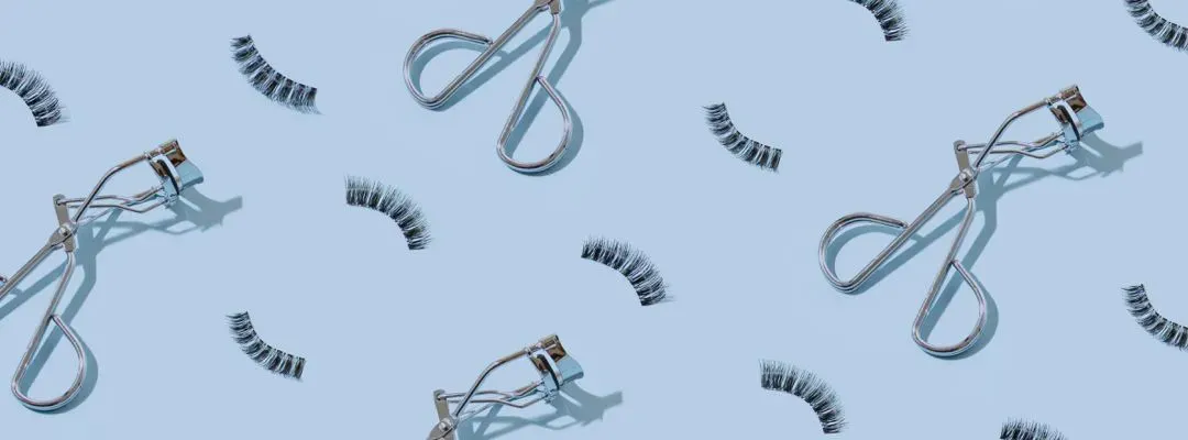 Fake eyelashes and eyelash curlers on a light blue background