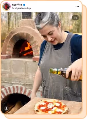 claire saffitz pouring olive oil on pizza in front of outdoor stone fire oven