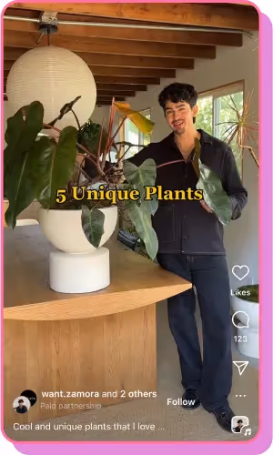 A man in a modern home smiles while showcasing unique houseplants on a wooden table