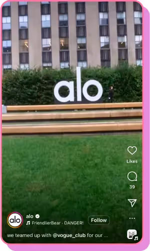 large "alo" sign sits in front of a modern building with greenery and wooden benches