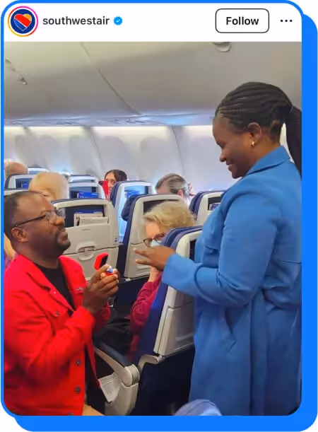 Man in red jacket proposing to a woman in blue coat inside an airplane cabin