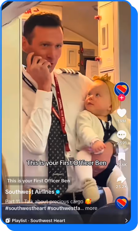 Airline pilot holding a baby while speaking into a phone near an airplane door
