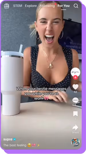 Woman laughing at a desk with a tumbler and phone in front of her.