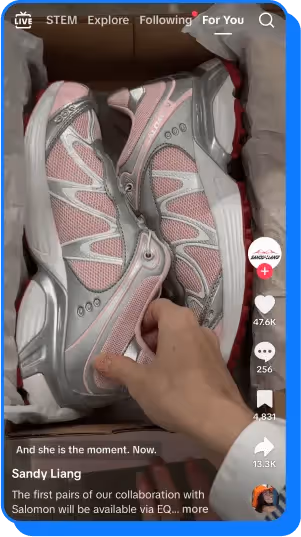 Hand holding pink and silver Sandy Liang x Salomon sneakers inside a shoebox