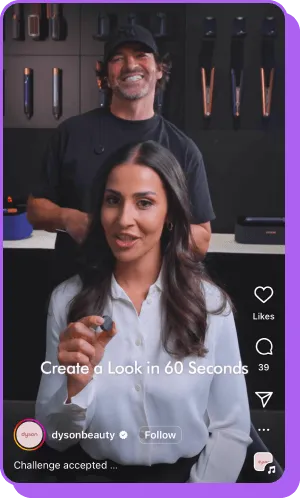 Woman demonstrating Dyson hair tool with hairstylist in background