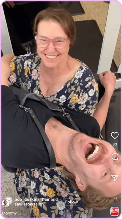 Smiling person in floral dress holds laughing man upside down in playful barbershop scene.