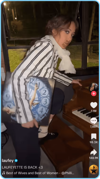 Woman in striped blazer posing by a piano while holding a ballet-themed clock bag.