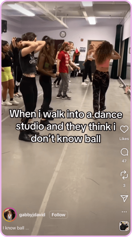 Dance class participants practicing choreography in a studio with mirrors and wood floors.