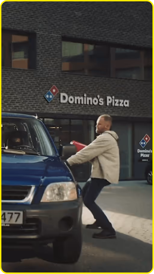 commercial showing man delivering pizza to a car outside a Domino’s Pizza storefront