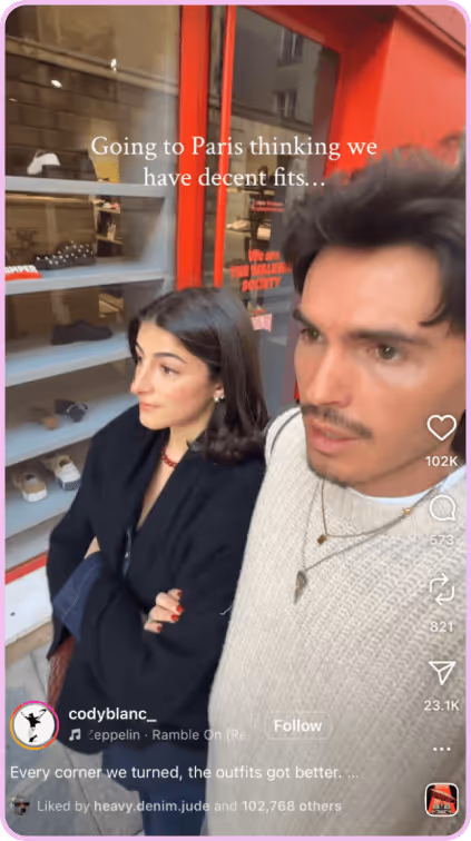 Man and woman standing on a Paris street, reacting to fashionable outfits around them.