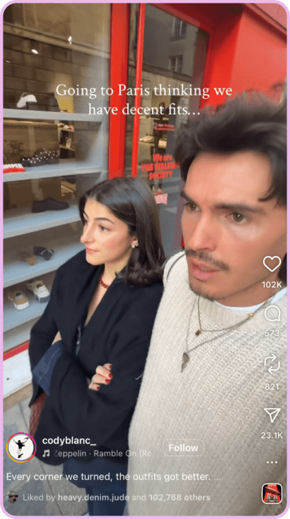 Man and woman standing on a Paris street, reacting to fashionable outfits around them.