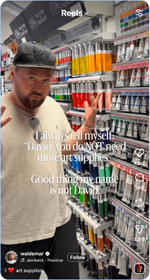 Artist standing in art supply store aisle filled with colorful paint tubes
