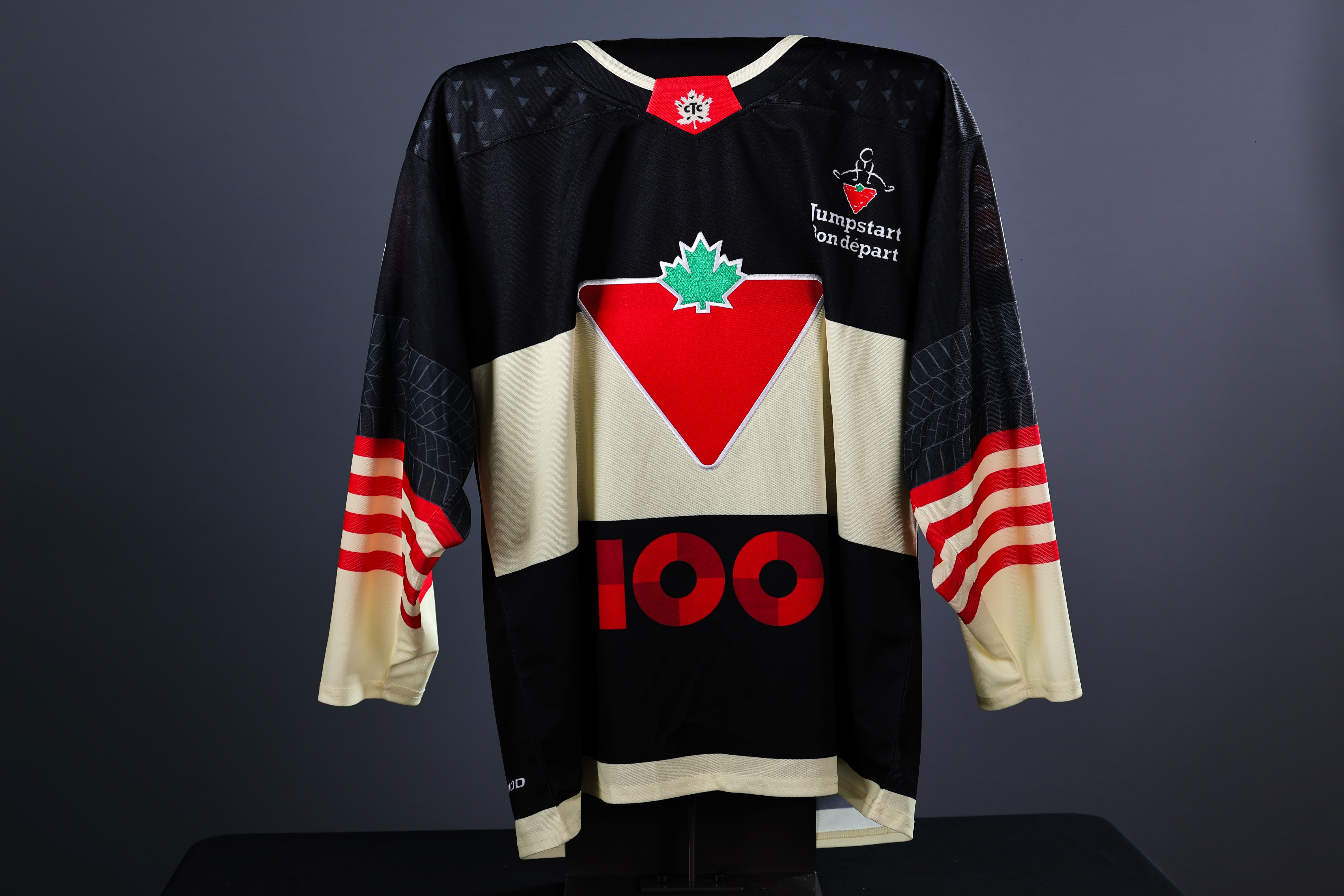 Black and cream-coloured ice hockey jersey with Canadian Tire logo on the front centre, the number "100" below, and the Jumpstart logo on the upper right chest. The back of the same black ice hockey jersey shows the name “BILLES” in bold white letters.