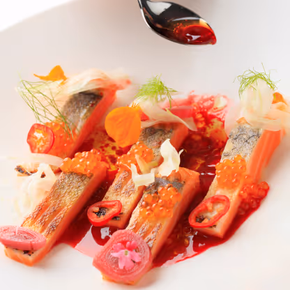 Gourmet salmon dish with roe, sliced chilies, herbs, and red sauce on white plate.