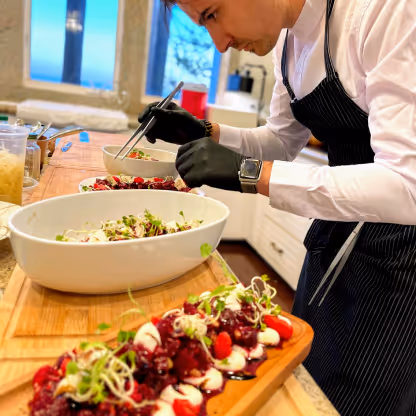 Chef wearing black gloves carefully plating gourmet salad dishes on a wooden counter in a kitchen.