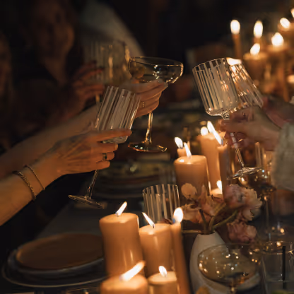 People raising glasses in a toast over a candlelit table with flowers and plates.