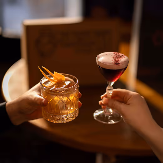 Two hands, raising a cocktail to one another