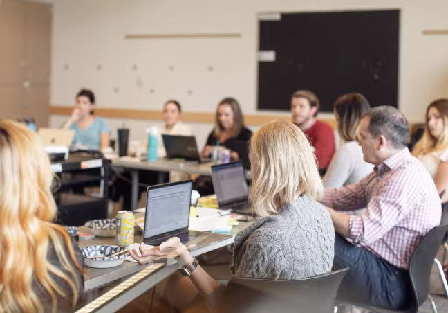 Team members actively participating in a collaborative meeting at Artemis Connection, with multiple laptops and materials present