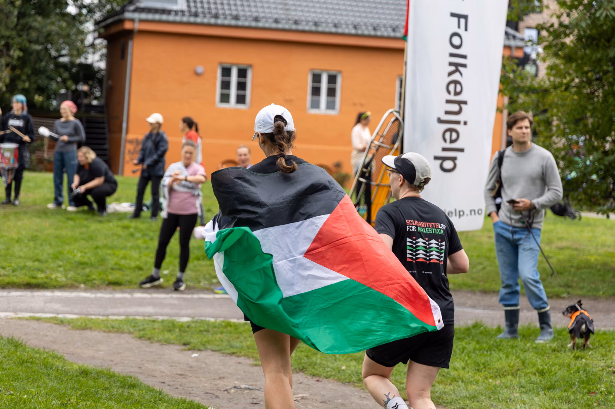To personer jogger mot mål, én med palestina-flagg over skuldrene. Sett bakfra.